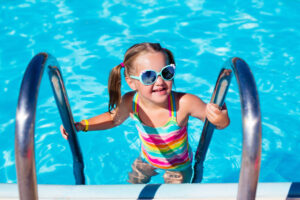 Kleines Mädchen steigt Poolleiter herauf im Schwimmbad.