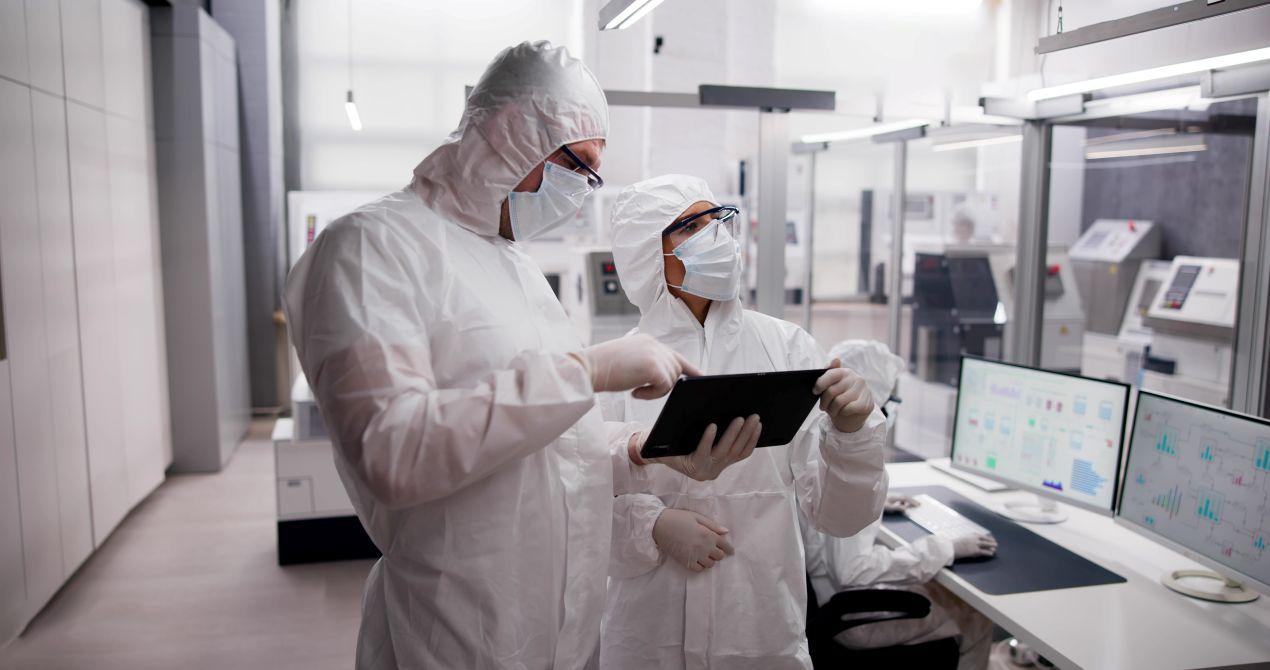 Mitarbeiter in Schutzkleidung kontrollieren Reinraumreinigung auf digitalen Displays in Produktionsumgebung