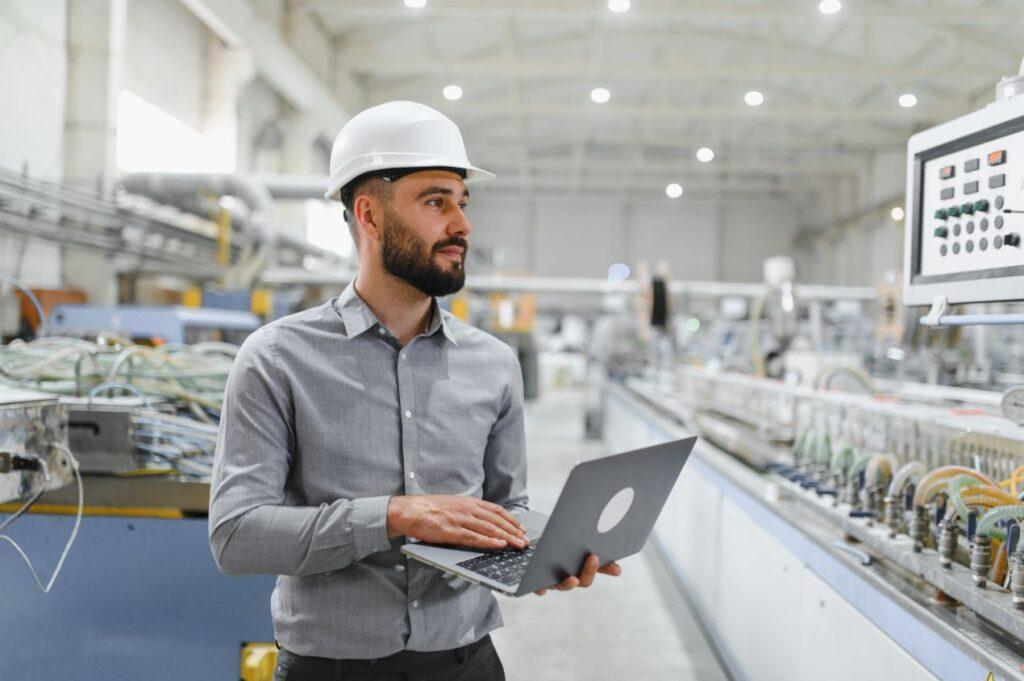 Ein Ingenieur mit Laptop ueberwacht eine automatisierte Fertigungslinie in einer modernen Produktionshalle – Beispiel fuer angewandte Automatisierungslösungen.