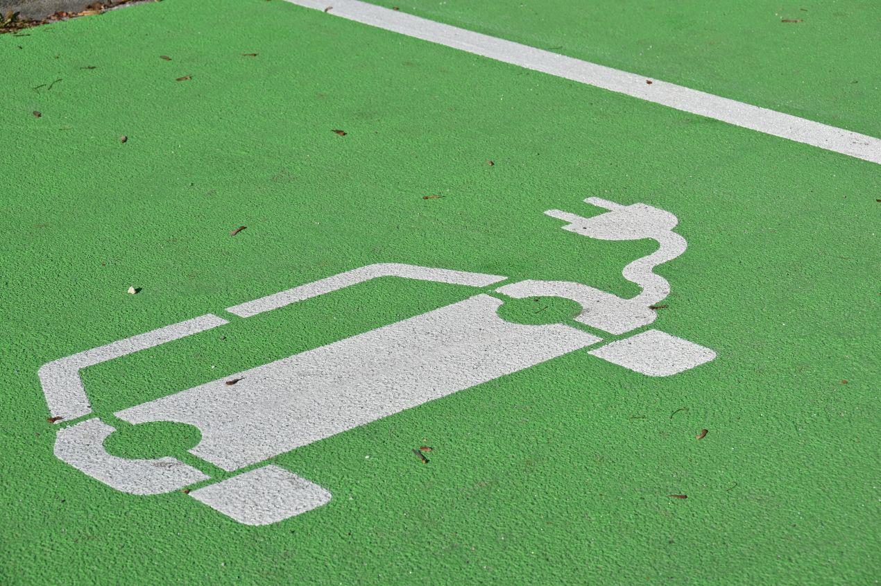 Weisses Elektroauto-Symbol auf gruener Bodenflaeche kennzeichnet Parkplatzmarkierung E-Auto fuer Ladezonen im oeffentlichen Raum.